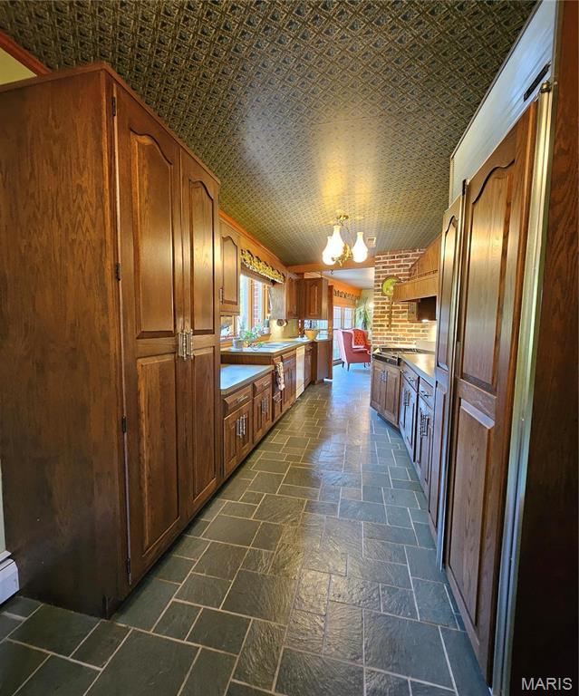 kitchen with a chandelier, stone tile flooring, a sink, brown cabinets, and light countertops