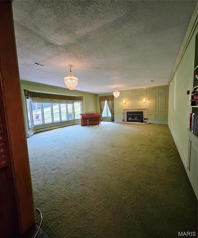 unfurnished living room with carpet floors, a chandelier, a glass covered fireplace, a textured ceiling, and ornamental molding
