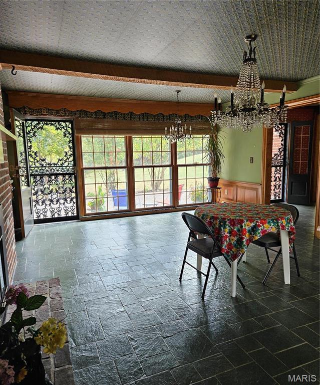 dining room with a chandelier, stone tile flooring, and wainscoting
