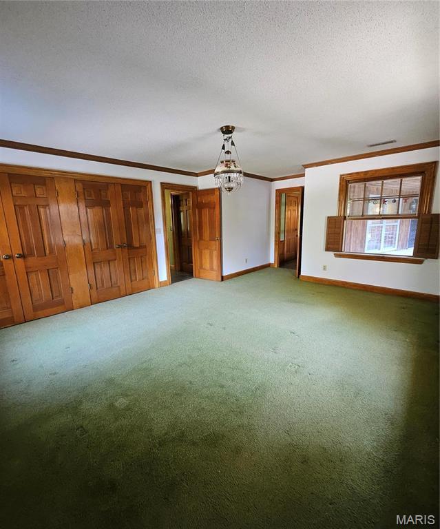 unfurnished living room with carpet, baseboards, crown molding, a chandelier, and a textured ceiling