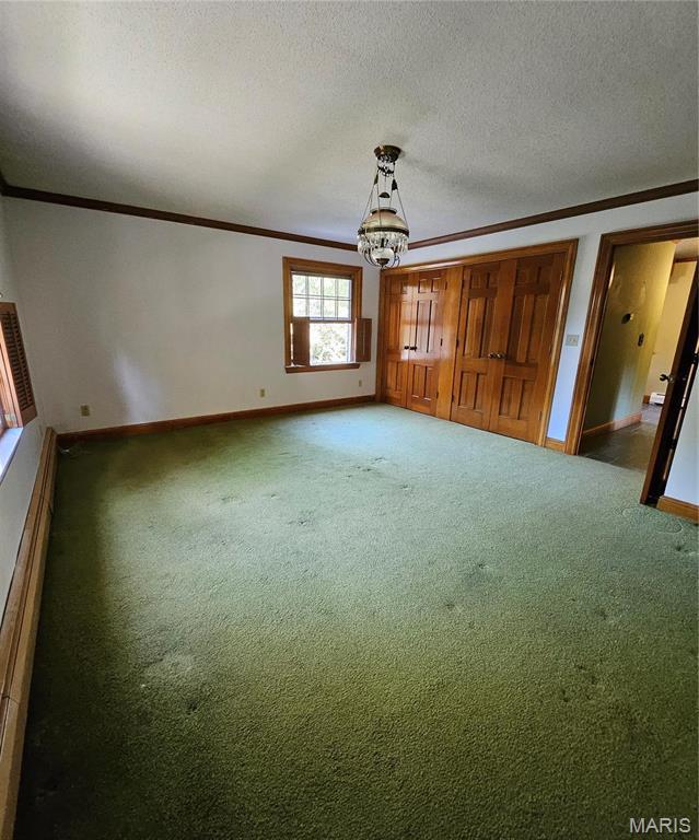 unfurnished bedroom with ornamental molding, baseboards, carpet flooring, a chandelier, and a textured ceiling
