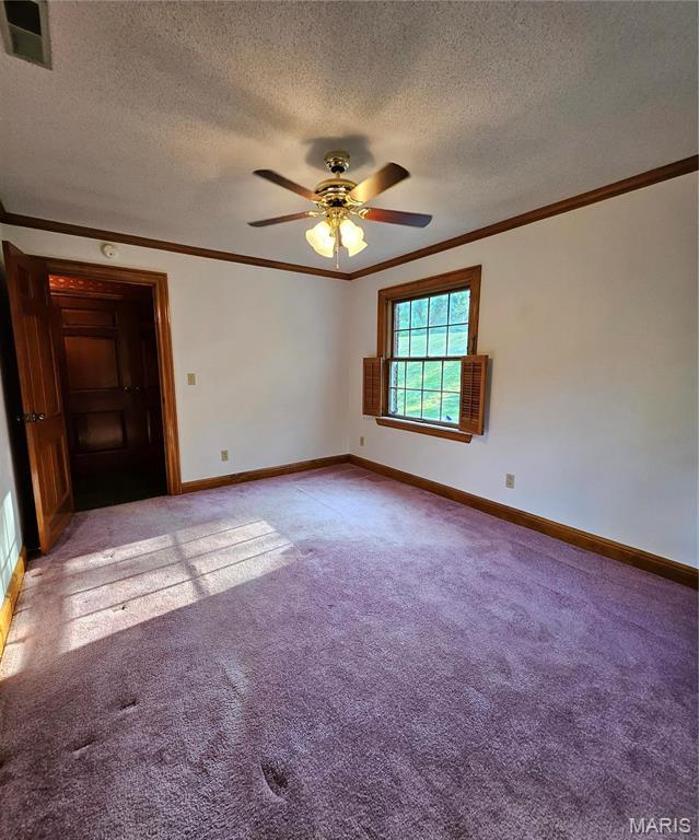 empty room with light carpet, ornamental molding, baseboards, ceiling fan, and a textured ceiling