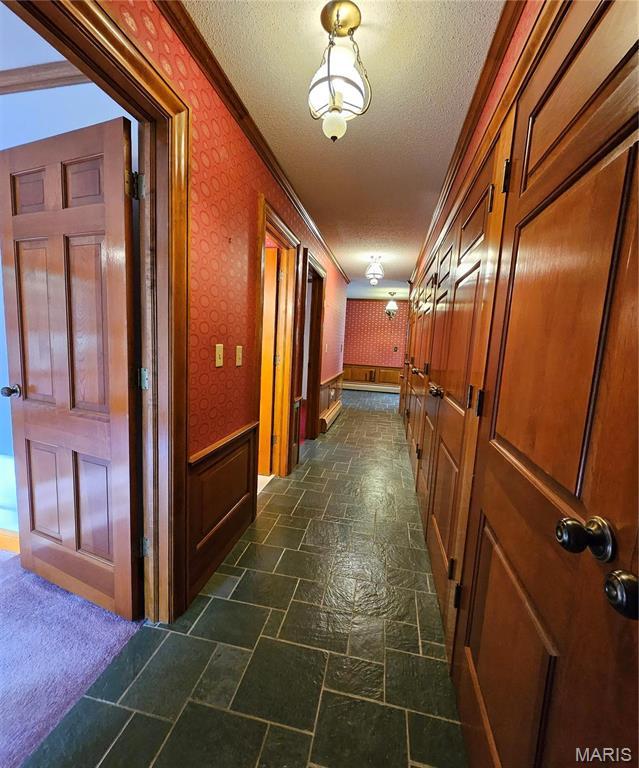 hallway with wallpapered walls, ornamental molding, a textured ceiling, and dark stone finish flooring