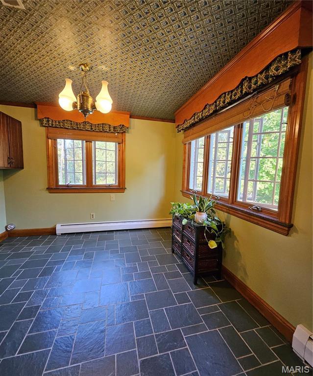 unfurnished dining area with a baseboard radiator, a chandelier, an ornate ceiling, ornamental molding, and baseboards