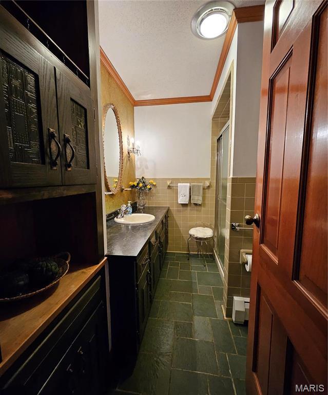 full bath with ornamental molding, a stall shower, vanity, tile walls, and a wainscoted wall