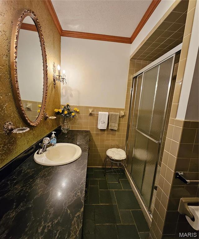 bathroom with tile walls, crown molding, a shower stall, vanity, and wainscoting