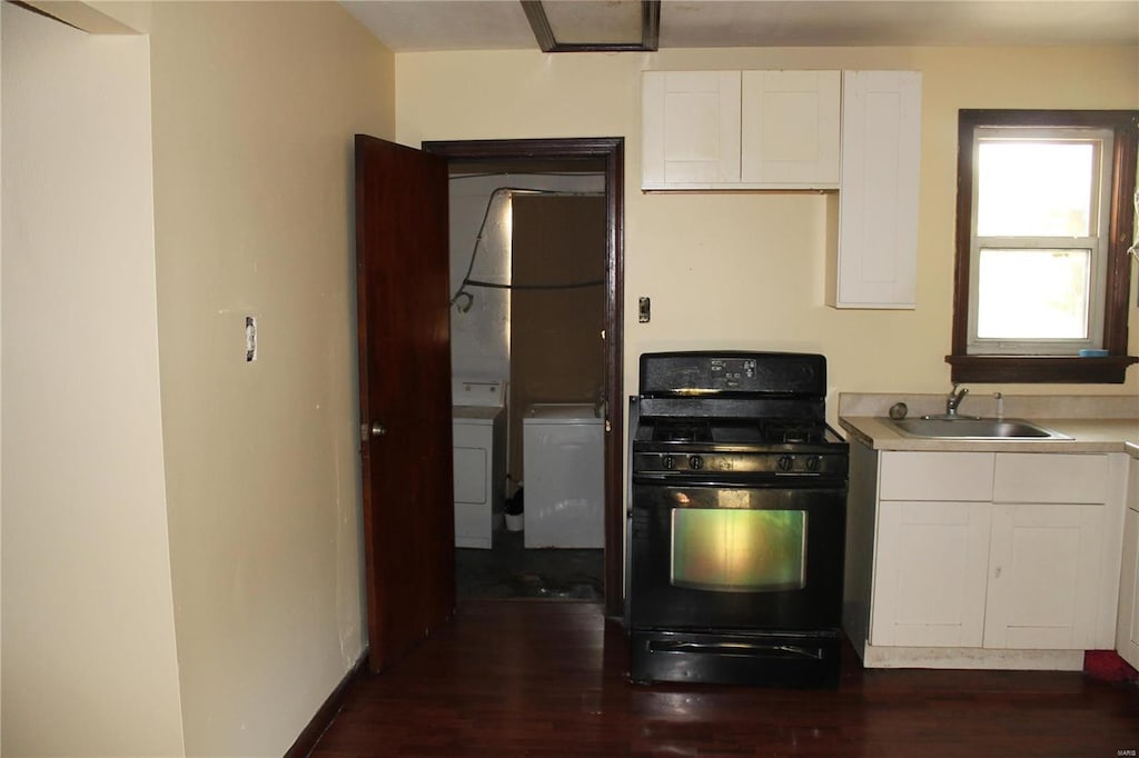 11814 Bellefontaine Rd, Saint Louis, MO 63138 - kitchen with black gas stove, a sink, washer / dryer, dark wood-style flooring, and white cabinetry