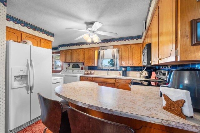 kitchen featuring appliances with stainless steel finishes, washer and clothes dryer, a sink, a peninsula, and brown cabinets