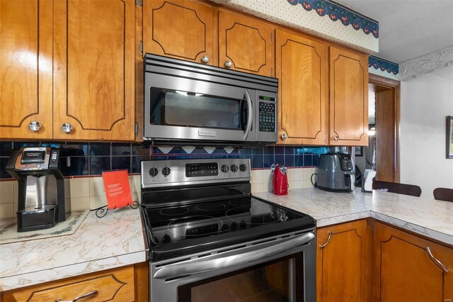 kitchen featuring stainless steel appliances, brown cabinetry, backsplash, light countertops, and a peninsula