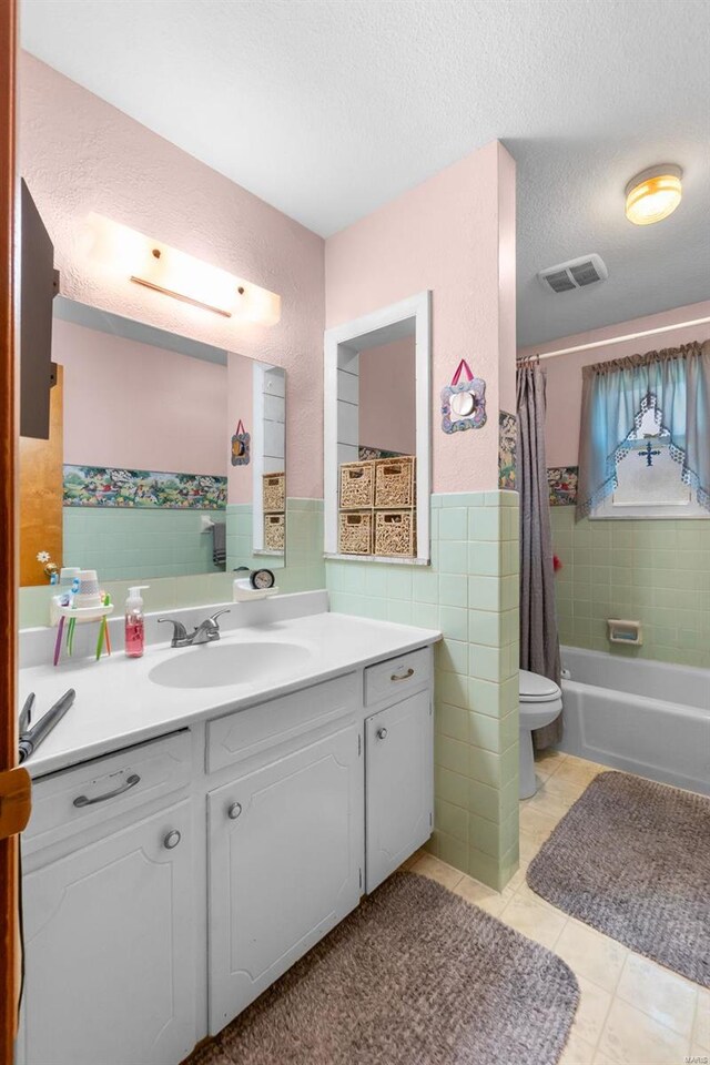 full bathroom with a textured ceiling, toilet, vanity, tile walls, and tile patterned flooring