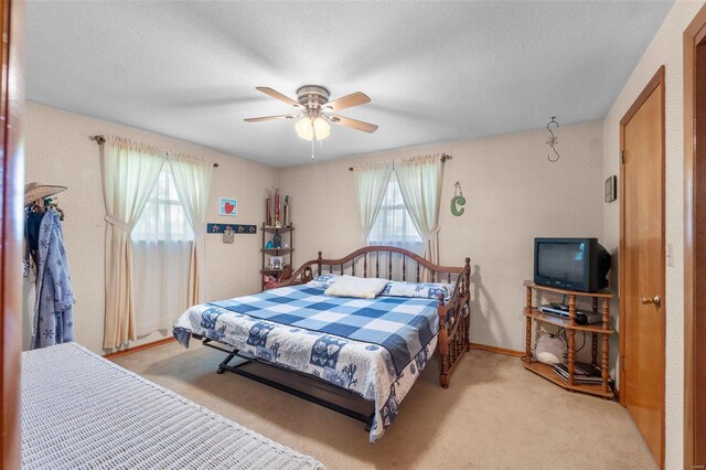 bedroom featuring a ceiling fan, light carpet, and a textured ceiling