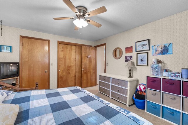 bedroom with wallpapered walls, carpet flooring, ceiling fan, and two closets