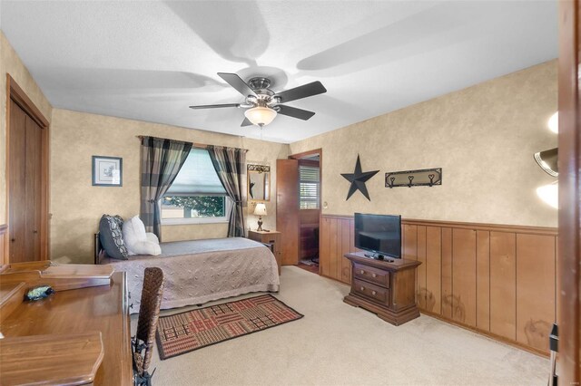 bedroom featuring light carpet, wainscoting, wooden walls, and a ceiling fan