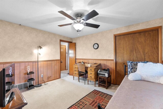 bedroom featuring wainscoting, wood walls, carpet flooring, and ceiling fan
