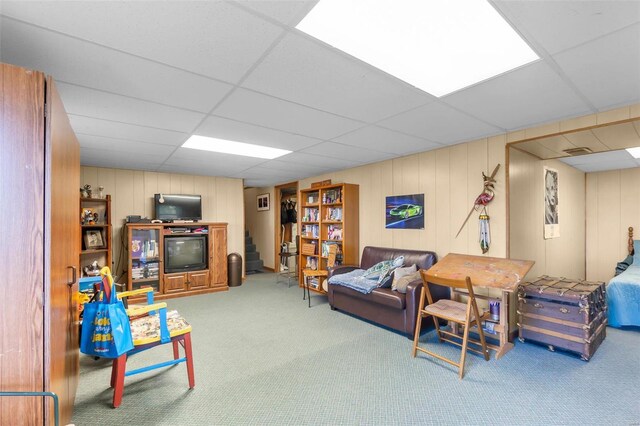 carpeted living room with a paneled ceiling and wood walls