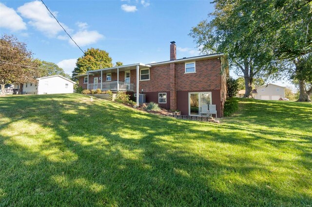 back of property with a chimney, a lawn, brick siding, and a porch