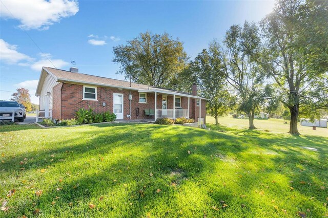 ranch-style house with brick siding, a front yard, a chimney, and covered porch