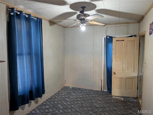 carpeted spare room featuring ceiling fan, crown molding, wooden walls, and baseboards