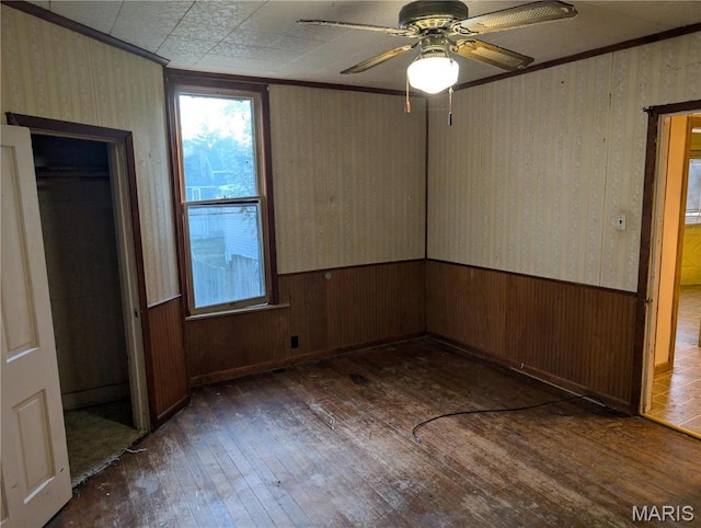 unfurnished bedroom with hardwood / wood-style floors, wallpapered walls, wainscoting, ornamental molding, and wooden walls