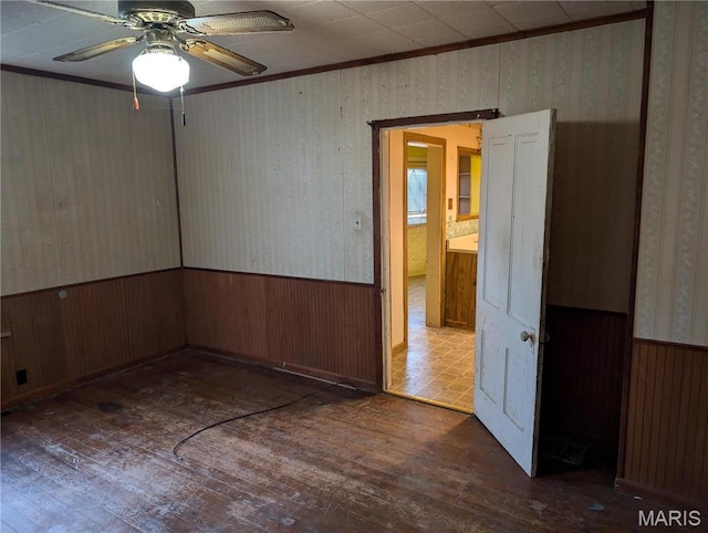 spare room featuring wood-type flooring, ceiling fan, wallpapered walls, crown molding, and wooden walls