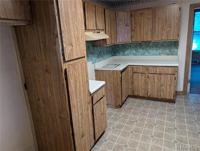 kitchen featuring under cabinet range hood, brown cabinets, and light countertops