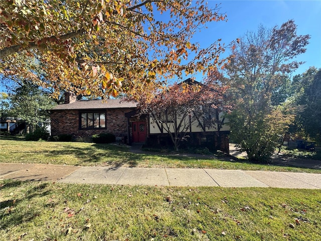view of front of house featuring a front lawn, a chimney, and brick siding