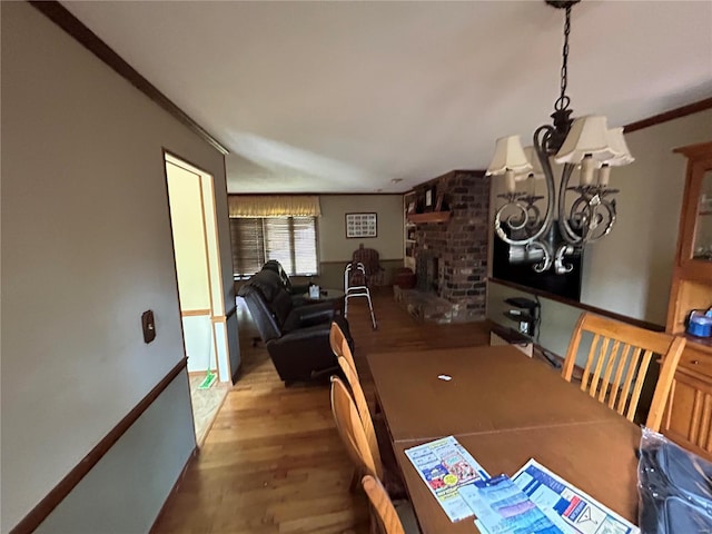 dining space featuring a chandelier, wood finished floors, a brick fireplace, and crown molding