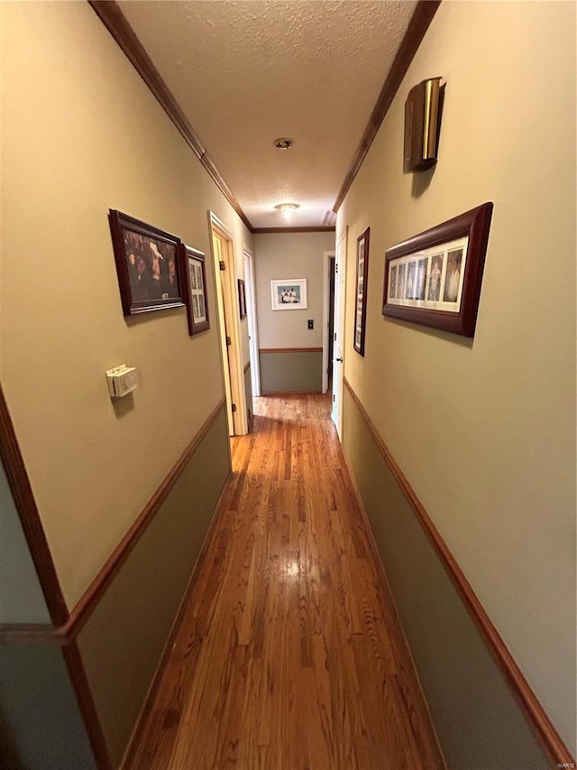 hall featuring ornamental molding, wood finished floors, and a textured ceiling