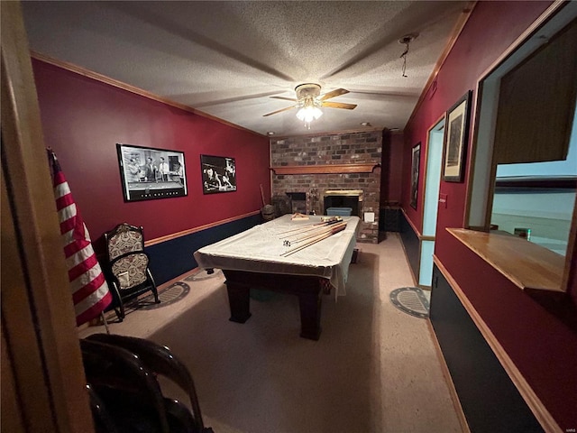 rec room with ceiling fan, billiards table, a textured ceiling, a brick fireplace, and ornamental molding