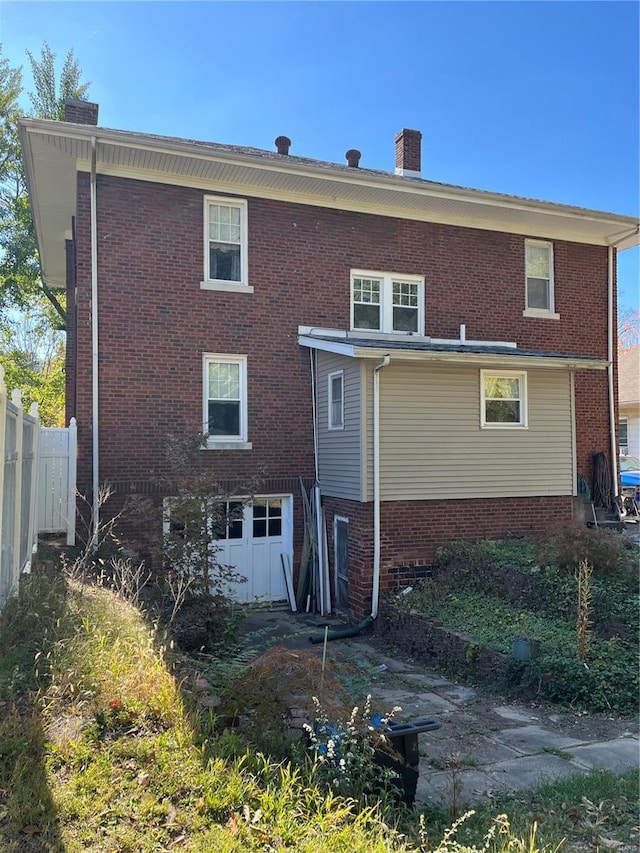 rear view of property with a chimney, fence, and brick siding