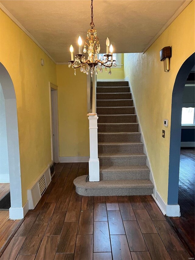 staircase with hardwood / wood-style flooring, arched walkways, ornamental molding, a chandelier, and baseboards