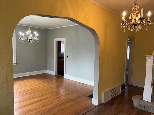 unfurnished dining area featuring arched walkways, a chandelier, ornamental molding, wood finished floors, and baseboards