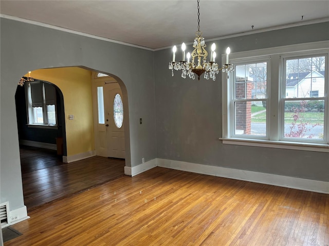 unfurnished dining area featuring arched walkways, a chandelier, light wood-type flooring, ornamental molding, and baseboards