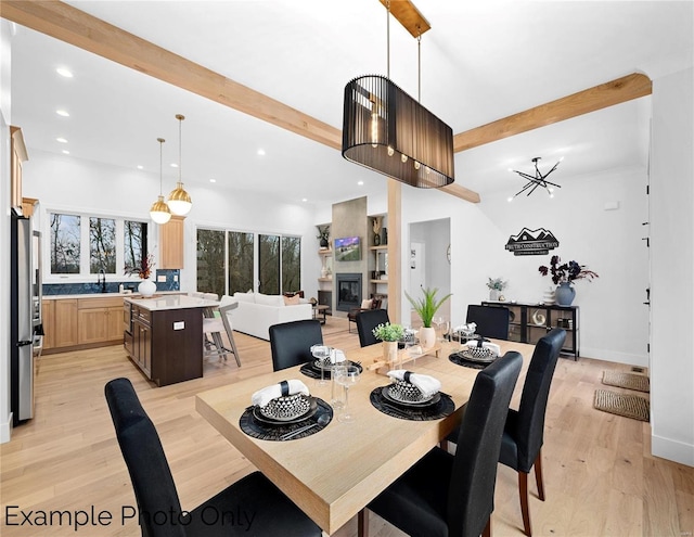 dining room with beam ceiling, recessed lighting, light wood-style floors, a glass covered fireplace, and baseboards