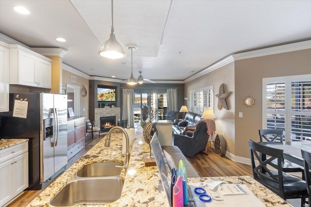 kitchen with stainless steel refrigerator with ice dispenser, a sink, open floor plan, wood finished floors, and ornamental molding