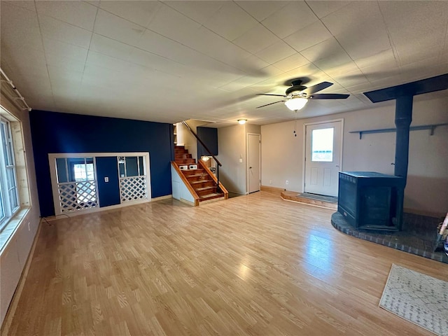 unfurnished living room with a wood stove, wood finished floors, stairway, baseboards, and a ceiling fan