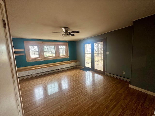 empty room with baseboard heating, wood finished floors, a ceiling fan, and baseboards