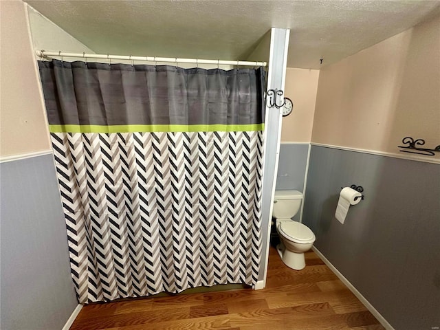 full bath featuring a wainscoted wall, wood finished floors, toilet, curtained shower, and a textured ceiling