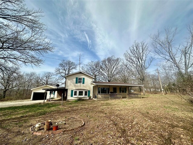 back of house with covered porch, dirt driveway, a carport, and a lawn
