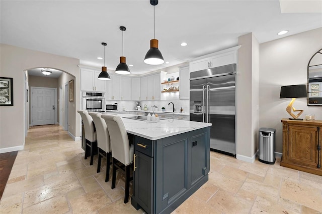 kitchen featuring stainless steel appliances, stone tile floors, arched walkways, white cabinetry, and recessed lighting