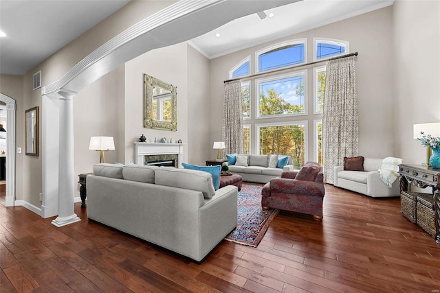 living area featuring ornate columns, dark wood-style floors, ornamental molding, a fireplace, and a high ceiling