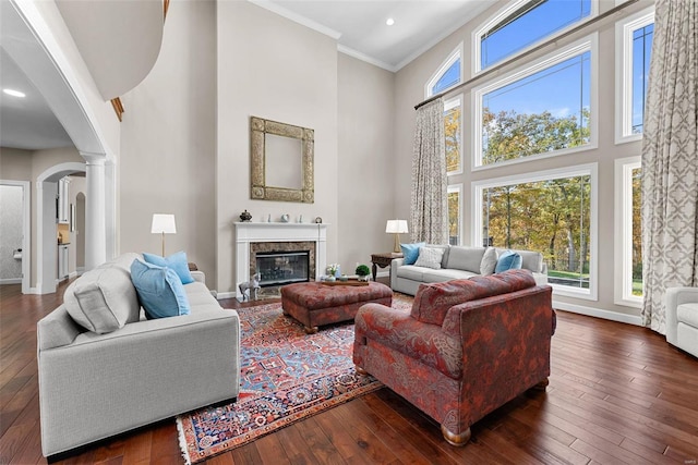 living room featuring a high ceiling, decorative columns, arched walkways, dark wood finished floors, and crown molding