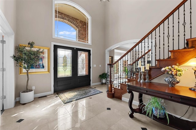 tiled foyer entrance with a towering ceiling, baseboards, arched walkways, and stairway