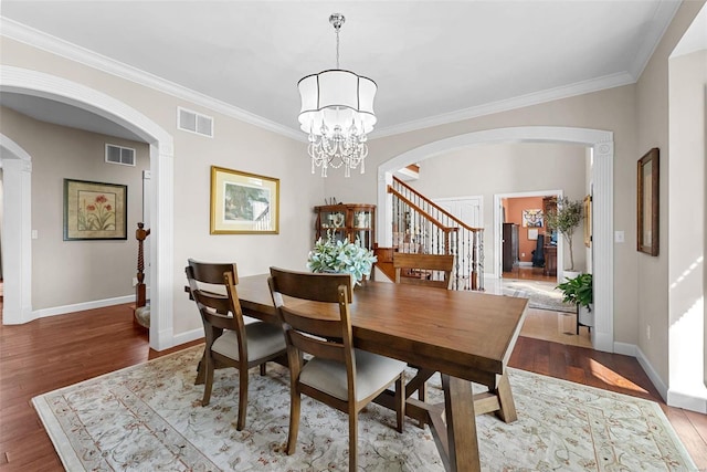 dining area featuring arched walkways, baseboards, crown molding, wood finished floors, and stairs