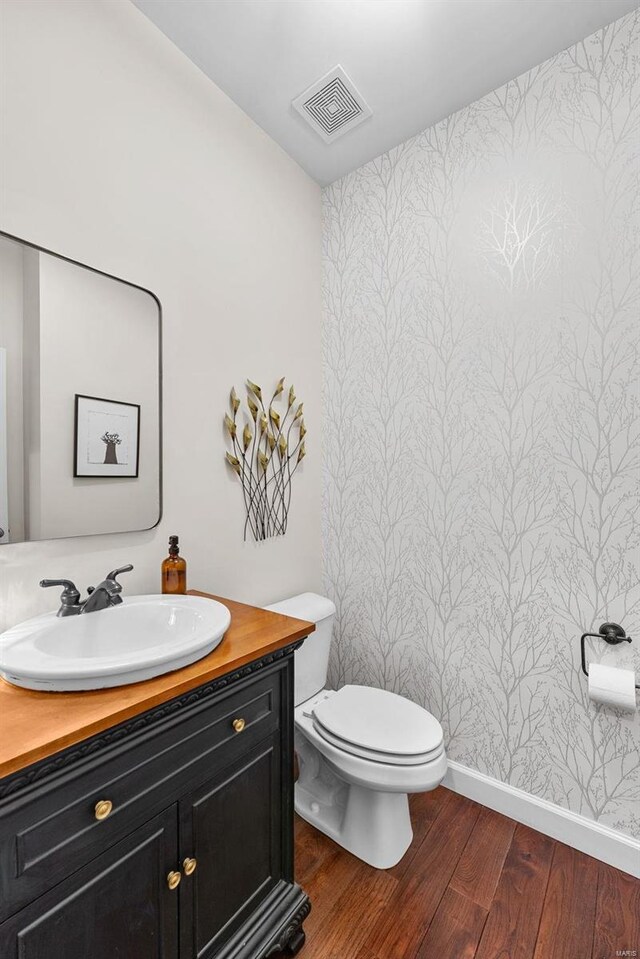 half bathroom featuring toilet, wood finished floors, and vanity