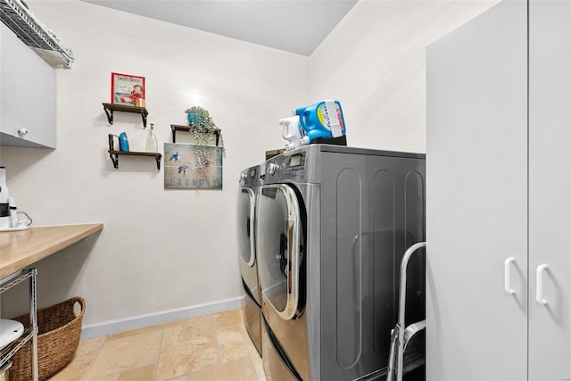 clothes washing area with cabinet space, washing machine and clothes dryer, baseboards, and stone tile flooring
