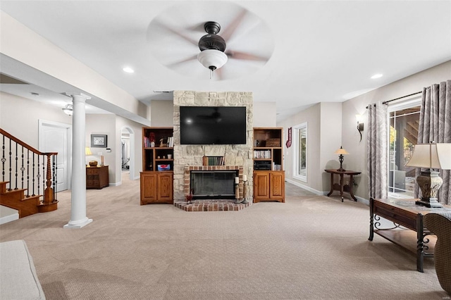 living room with light colored carpet, a ceiling fan, decorative columns, a stone fireplace, and baseboards