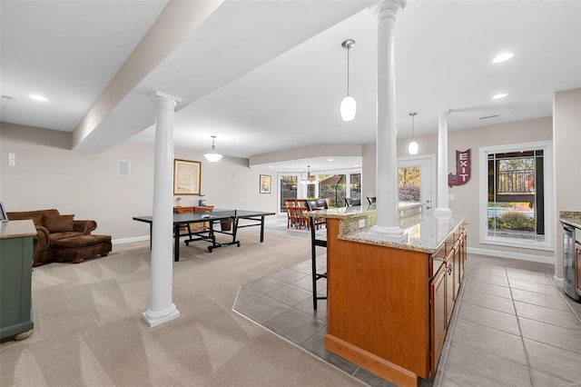 kitchen with ornate columns, open floor plan, brown cabinets, a kitchen breakfast bar, and light stone countertops