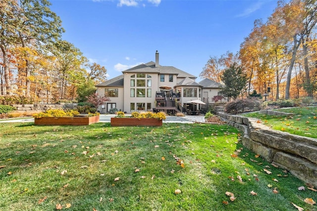 rear view of property with a vegetable garden, a wooden deck, a chimney, a sunroom, and a lawn