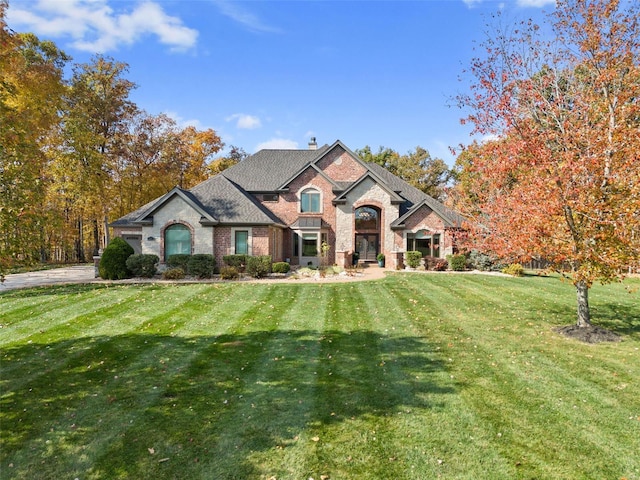 french country home featuring a chimney, a front yard, and brick siding